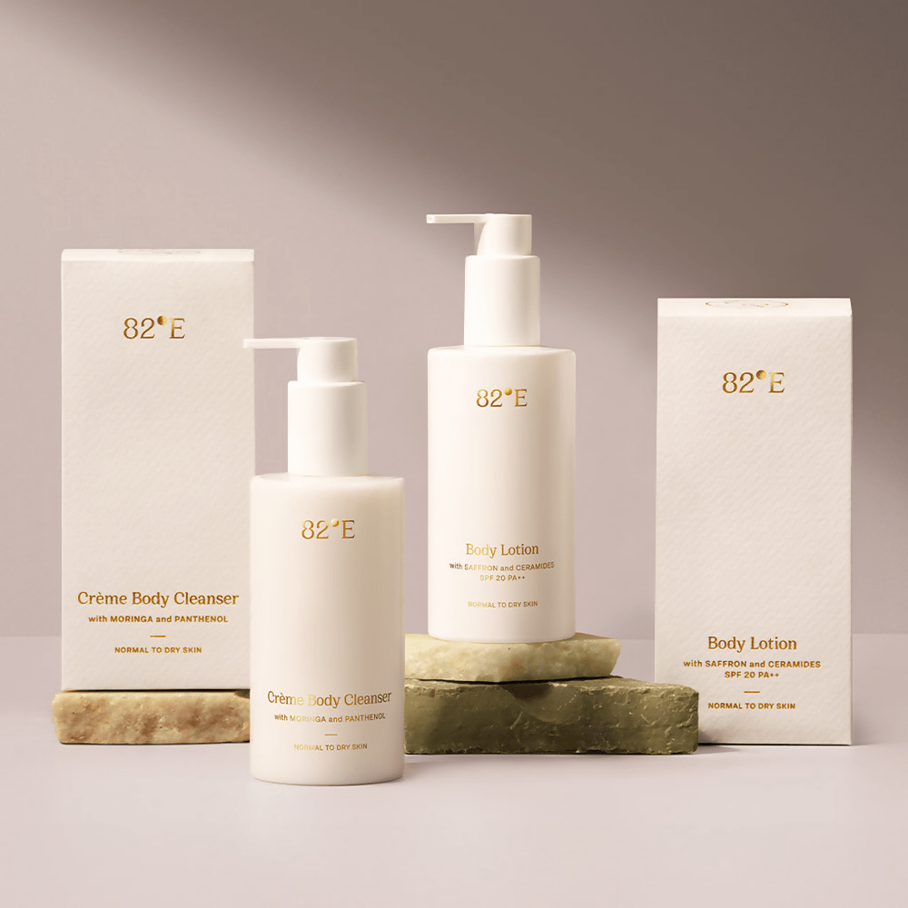 A collection of skincare products from 82°E, including a creme body cleanser and body lotion, packaged in white containers with the brand's logo.