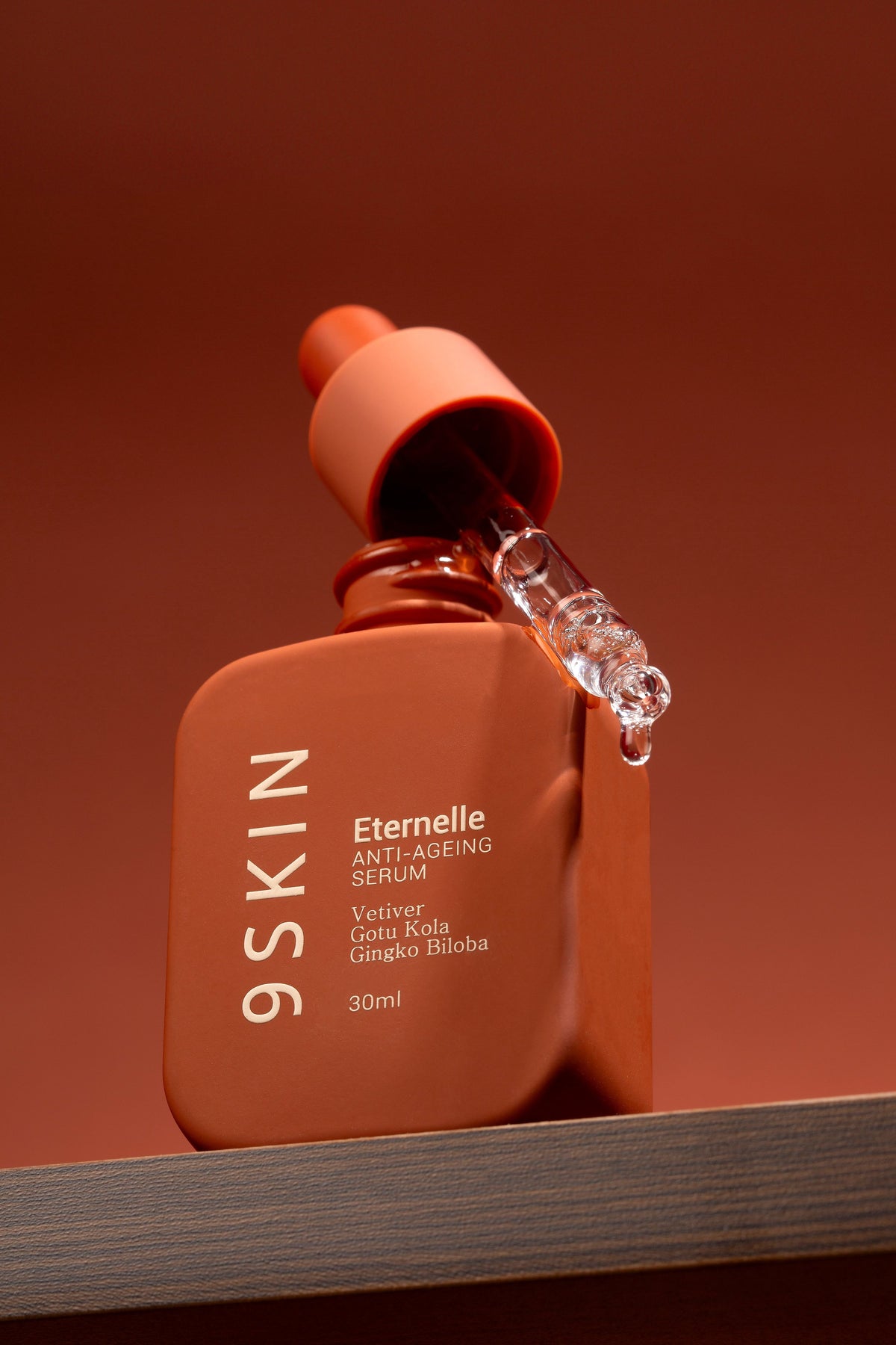 Orange skincare serum bottle with dropper on a brown background