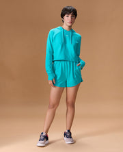 Person wearing a turquoise hoodie and shorts set on a beige background