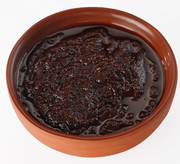 Dark brown jam in a terracotta bowl on a white background