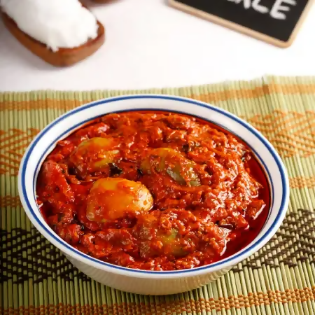 Bowl of red curry with vegetables on a textured mat