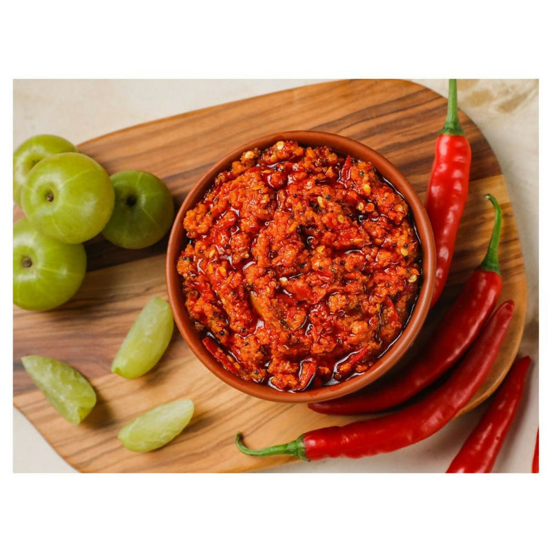 Bowl of red chili paste on a wooden board with green plums and red chilies.
