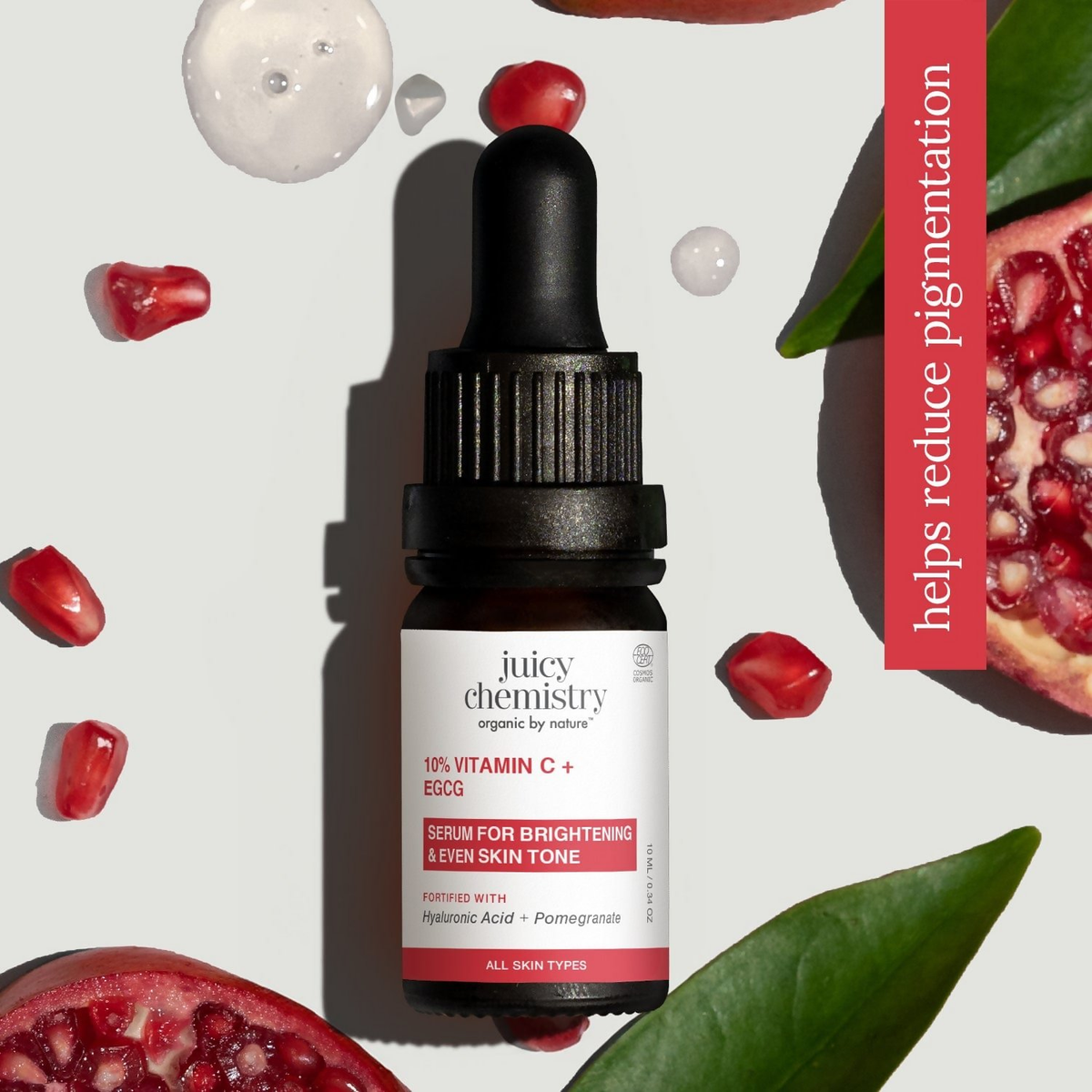 Juicy Chemistry vitamin C serum bottle with pomegranate seeds and leaves on a light background
