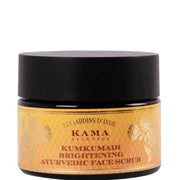 A jar of Kama Ayurveda Kumkumadi Brightening Ayurvedic Face Scrub with a black lid and a label that has gold and white design elements.