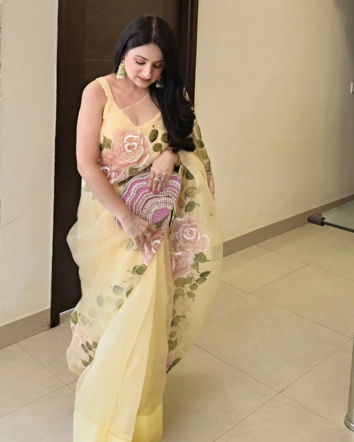 Woman wearing a yellow saree with floral patterns indoors.