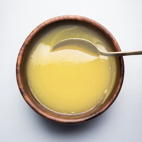 Bowl of yellow liquid with a spoon on a light gray background