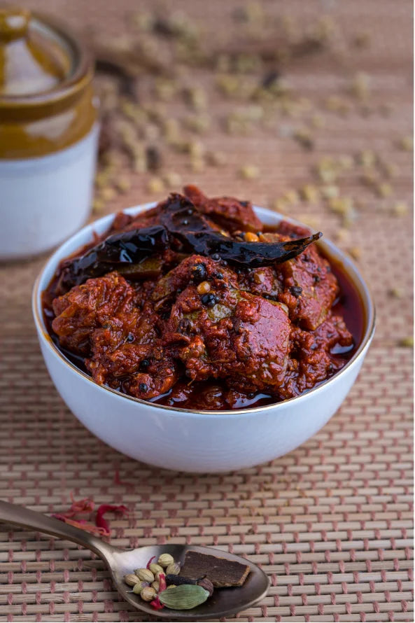 Spicy curry in a white bowl with spices on a wooden surface