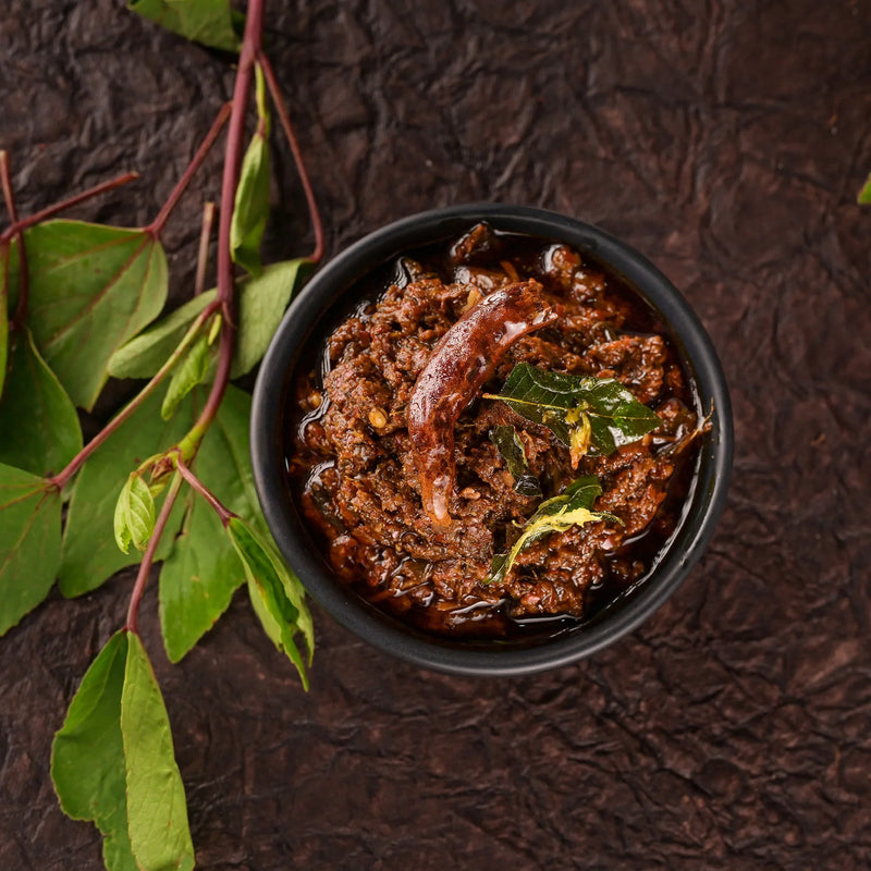Dark bowl of curry with green leaves on a textured dark background