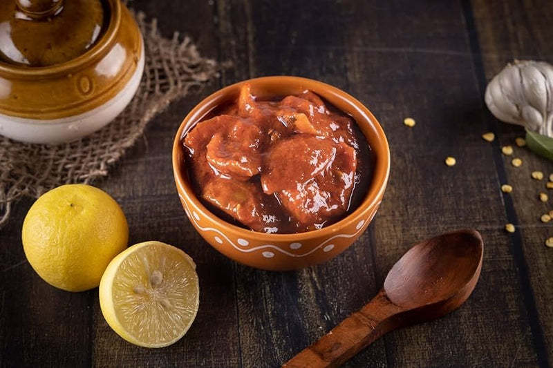 Bowl of red stew with lemons and a wooden spoon on a dark surface