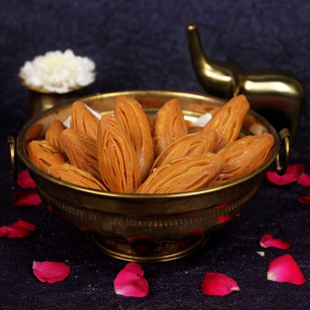Dried fruits in a brass bowl with pink petals on a dark background