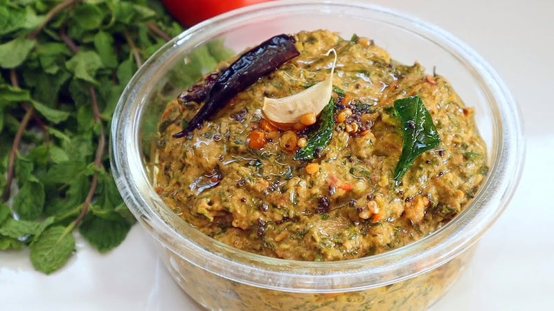 Jar of green pesto with herbs and a red chili pepper on a white background