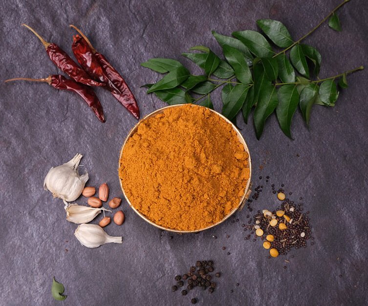 Spice blend in a bowl with red chilies, garlic, and leaves on a dark surface