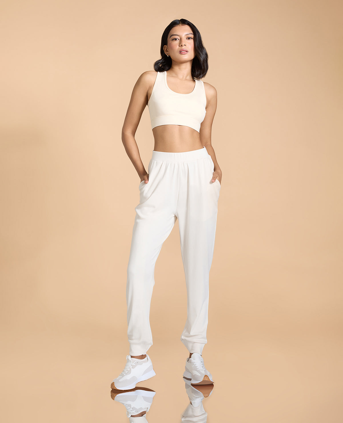 Woman wearing a white sports bra and pants on a beige background