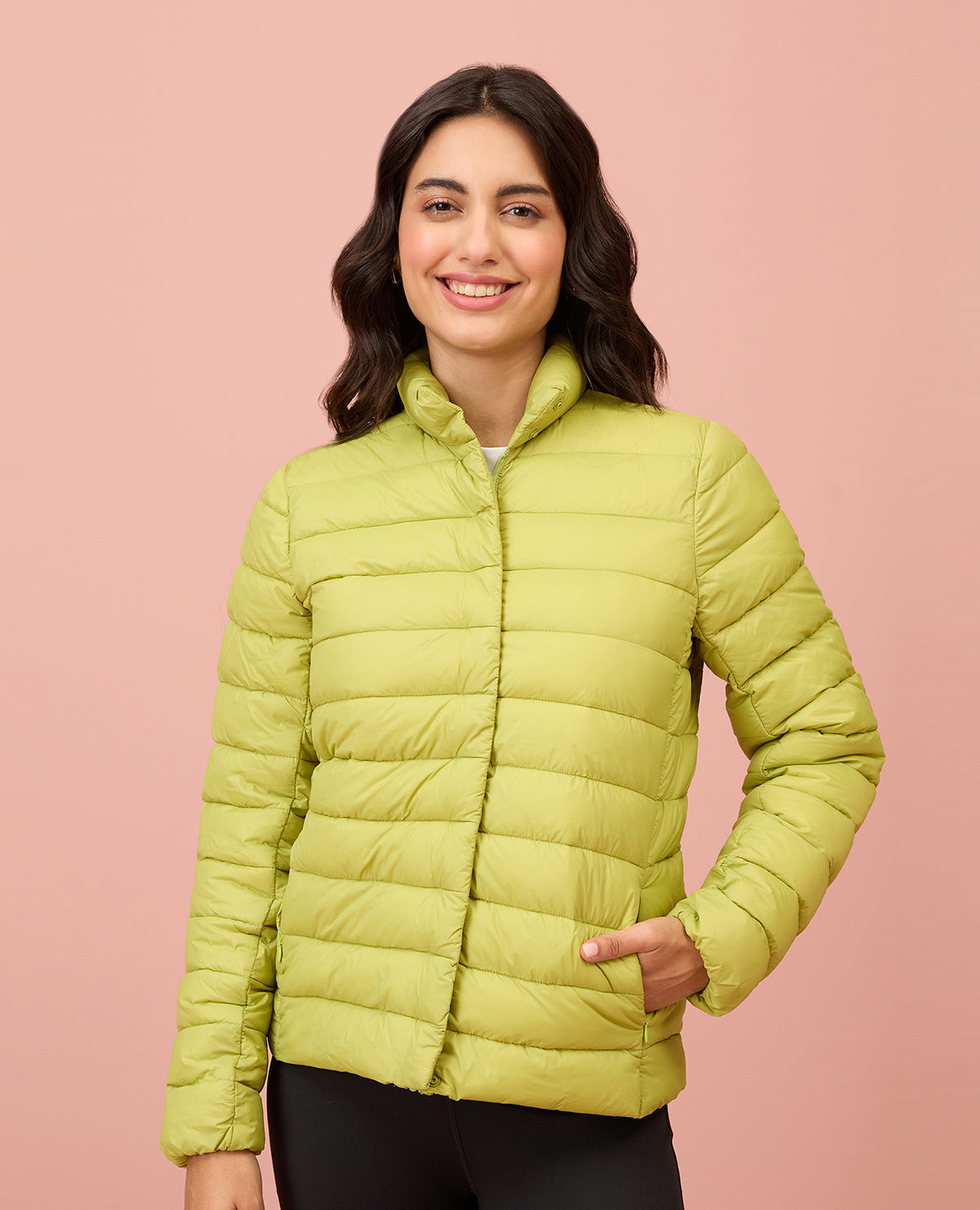 Woman wearing a light green puffer jacket against a pink background