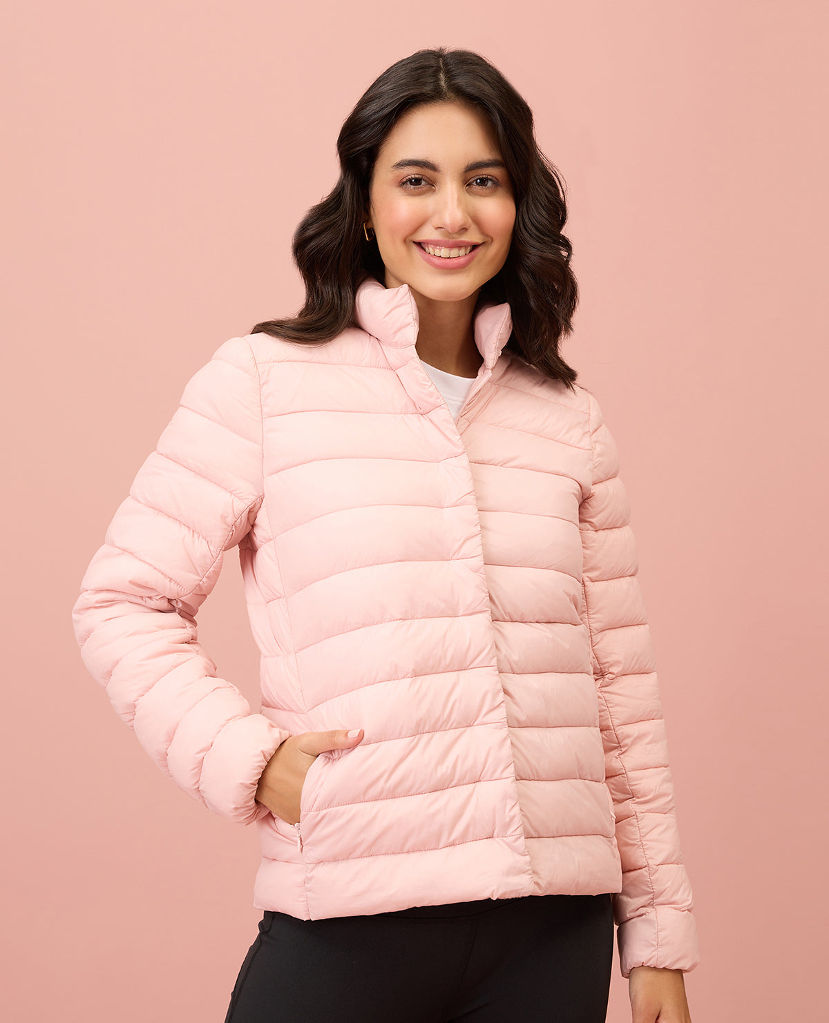 Woman wearing a pink puffer jacket against a pink background