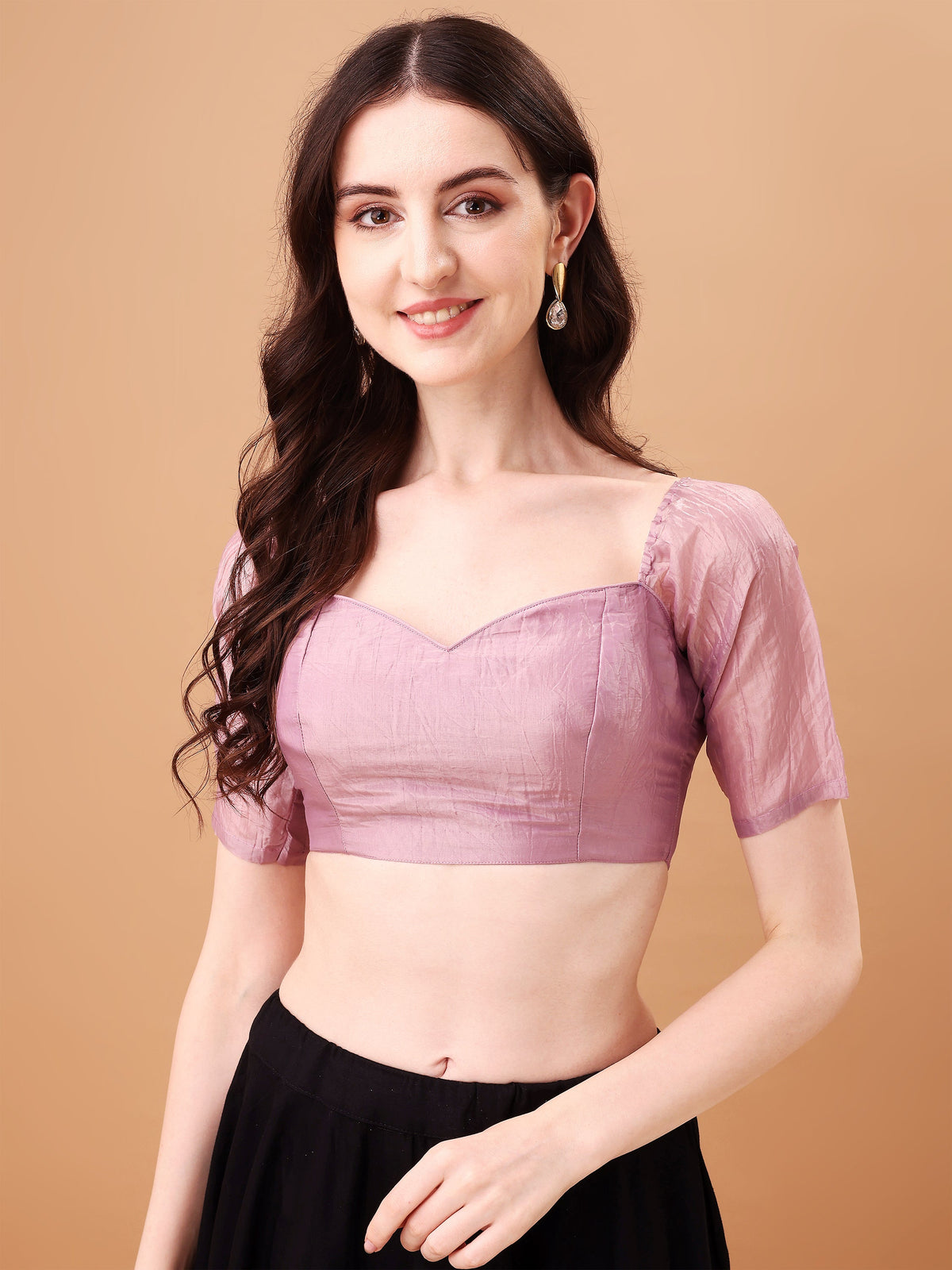 Woman wearing a pink blouse with sheer sleeves against a beige background