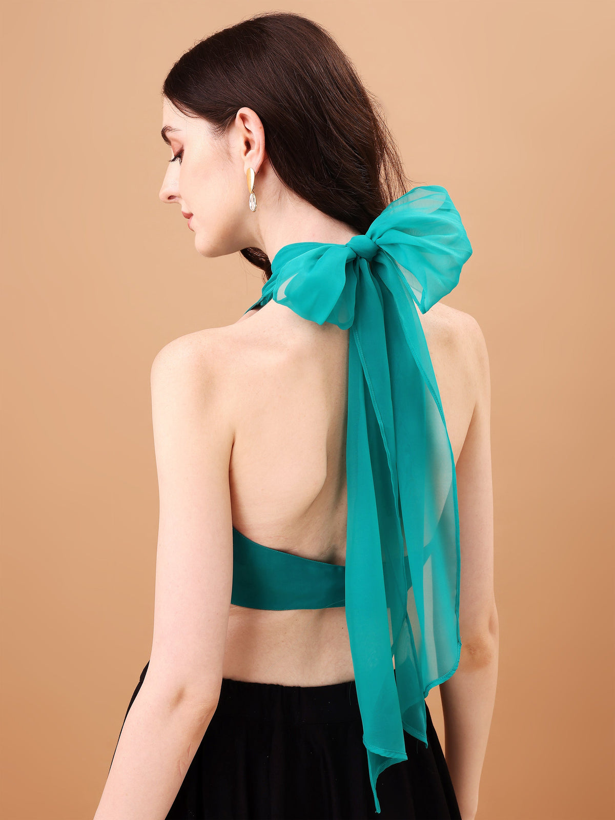 Woman wearing a teal halter top with a matching scarf on a beige background