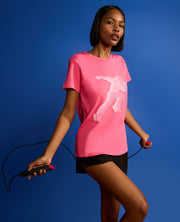 Woman in pink t-shirt and black shorts holding a jump rope against a blue background
