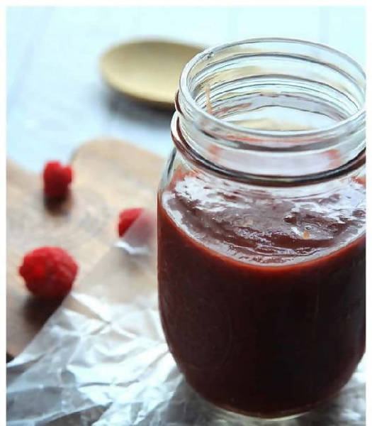 Jar of red sauce with raspberries on a wooden surface