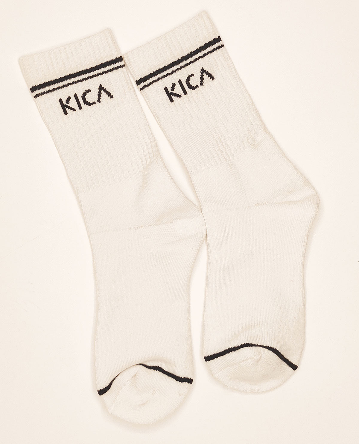 Pair of white socks with black trim and 'KICA' branding on a light beige background