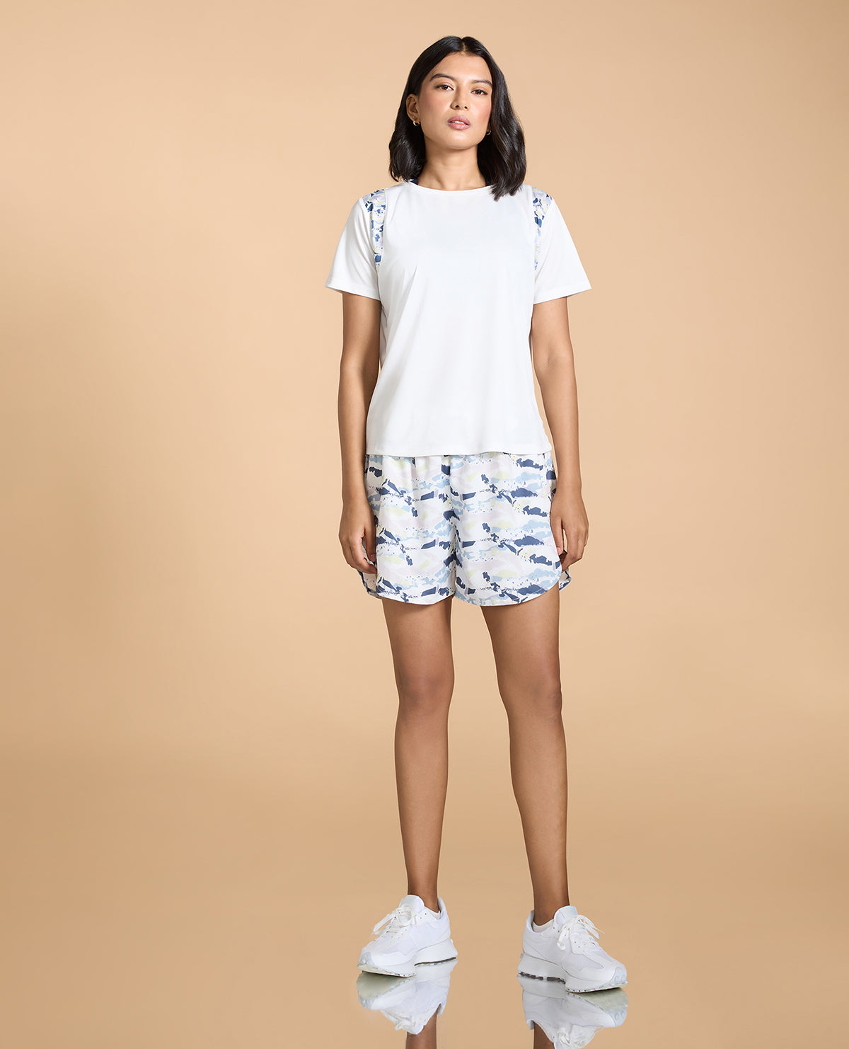 Woman wearing a white t-shirt and patterned shorts on a beige background