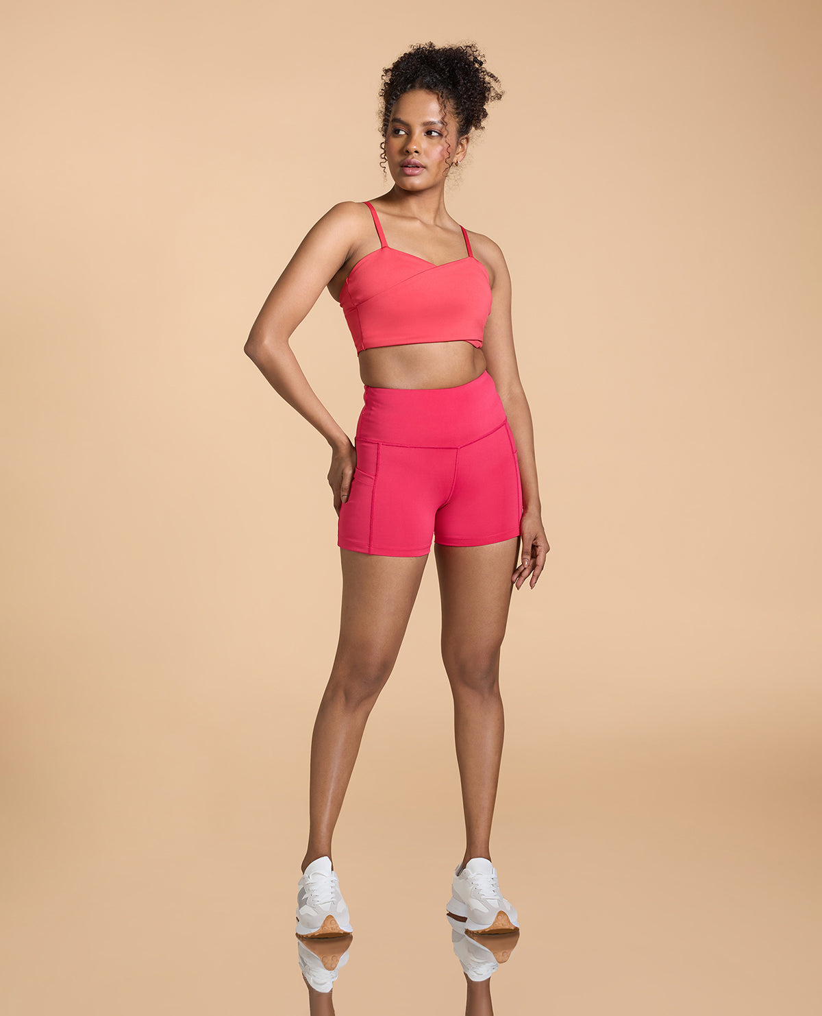 Woman wearing a pink sports bra and shorts set on a beige background