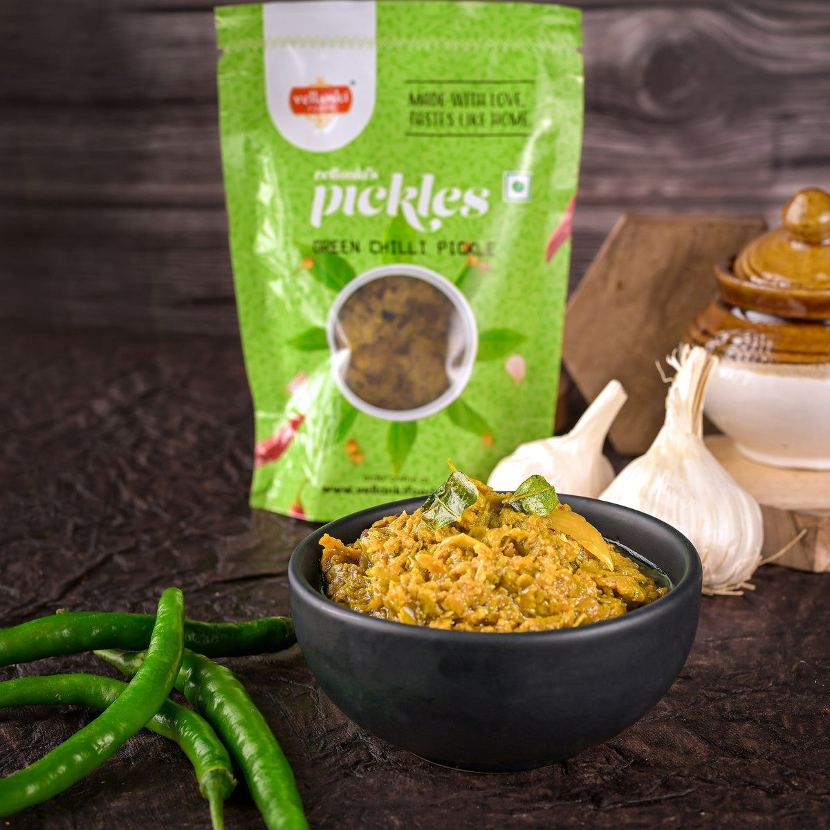 Green packet of pickles with a bowl of pickled green chili on a wooden surface.