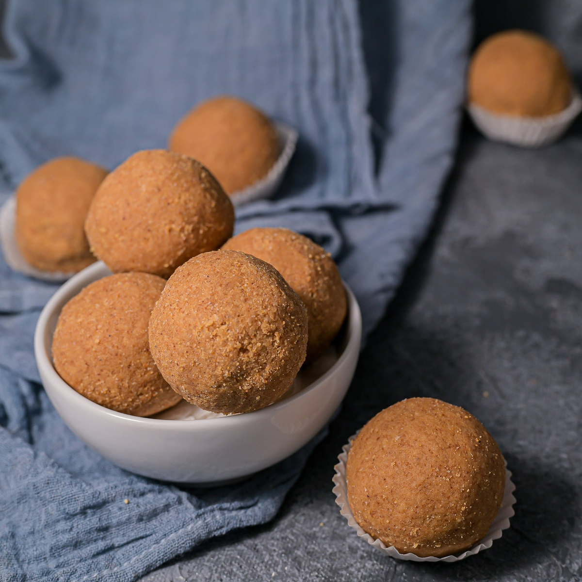 Bowl of brown spherical cookies on a blue cloth with a gray background